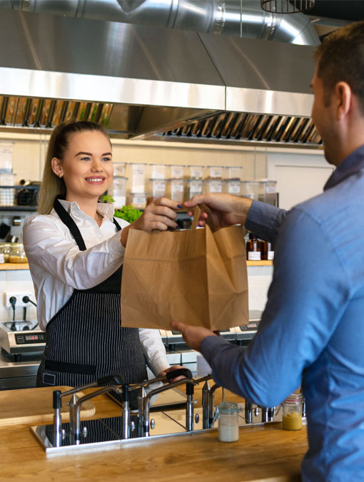 A woman hands a man a paper bag in a coffee shop.